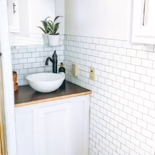 Lavabo moderno en cocina con azulejos blancos y decoración minimalista. Planta en maceta.